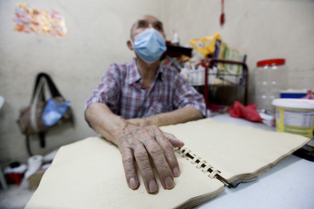 行动管制令期间无法外出工作，叶志明不忘拿出盲人按摩手册来复习，分秒不空过。 【摄影：梁倩宜】