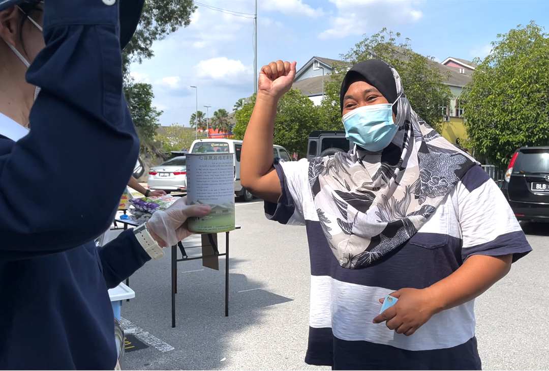 社区志工带领受惠者握拳高举做出加油的手势并高喊“Kita akan Selamat! Semua Orang Selamat! ”的口号，让发放现场增加了一股正气。 【摄影：胡永雄】
