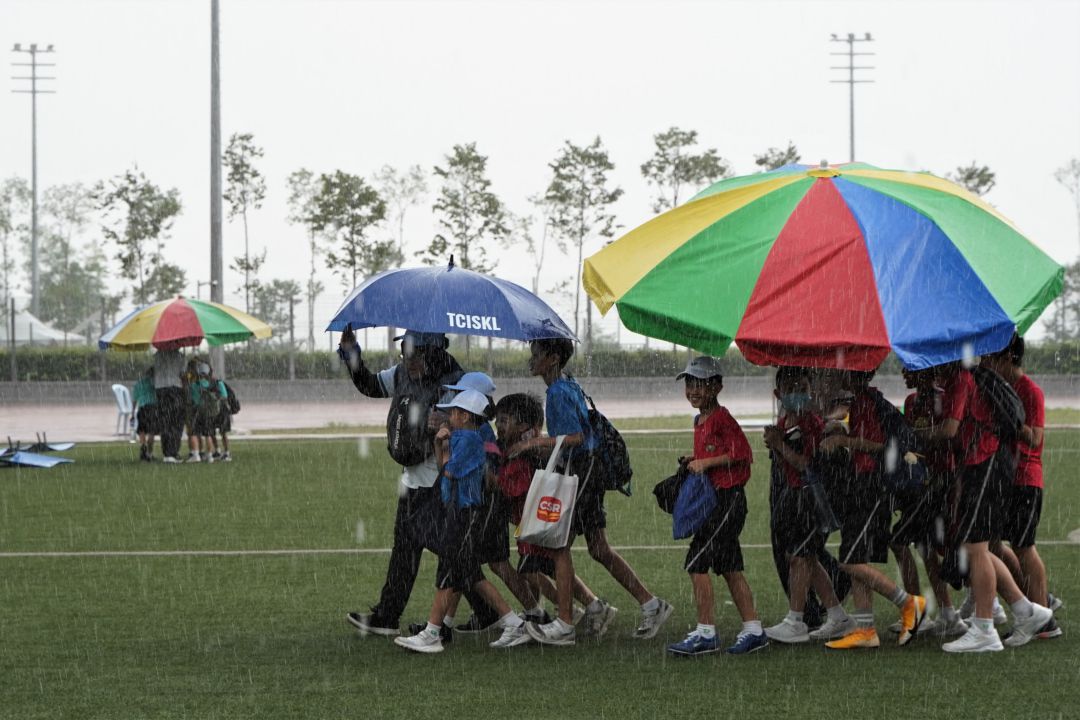 大雨迫使户外运动停止。老师与家长赶紧撑着大伞为孩子们遮风挡雨，将学生送往学校礼堂避雨。 【摄影：伍诗昱】