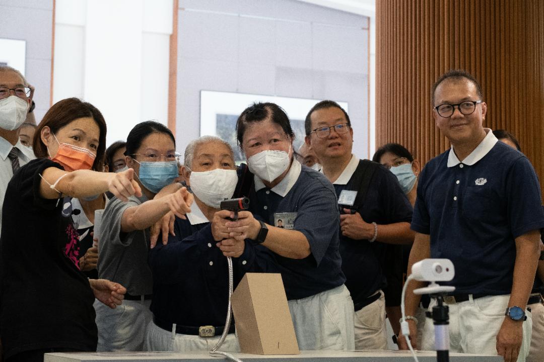 An elderly visitor aiming to shoot the mosquito larvae at the “Crime Scene” with guidance from an assistant researcher from the NSTM exhibition team (1st from left) and volunteers. [Photo by Lee Kok Keong]
