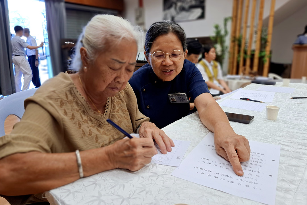 参与“一书一茶2.0”的会众邓玉梅，在志工黄秋玉的陪伴下，用心抄写静思语。【摄影：黄秀珍】