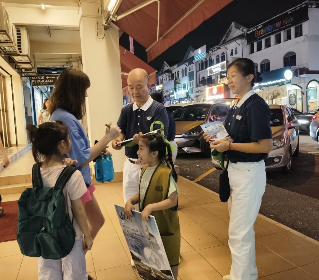 黄建基八岁的孙女黄书宁（右二着志工背心者）巧遇同学和妈妈一起购物，她主动上前邀约，接引了同学的妈妈加入浴佛行列。 【摄影：张丽诗提供】